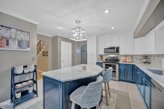 kitchen with appliances with stainless steel finishes, blue cabinetry, a center island, white cabinetry, and hanging light fixtures