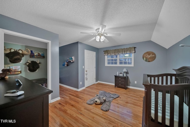 bedroom with lofted ceiling, ceiling fan, light wood-type flooring, a textured ceiling, and a nursery area