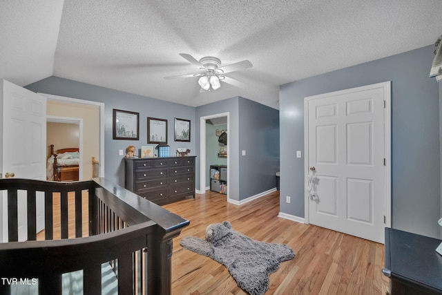 bedroom with a crib, a textured ceiling, light hardwood / wood-style flooring, and ceiling fan