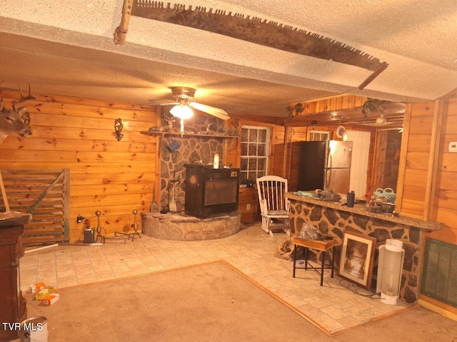 interior space with a wood stove, wood walls, ceiling fan, and a textured ceiling