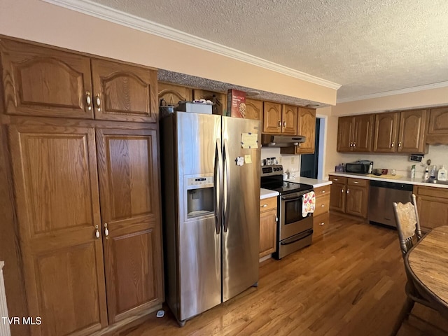 kitchen with a textured ceiling, wood-type flooring, ornamental molding, and appliances with stainless steel finishes