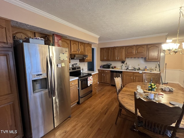 kitchen with stainless steel appliances, an inviting chandelier, crown molding, pendant lighting, and wood-type flooring