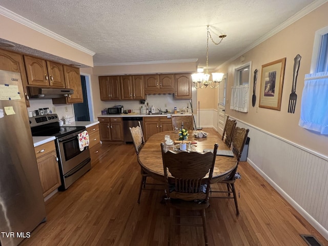 kitchen featuring wood-type flooring, stainless steel appliances, decorative light fixtures, and crown molding