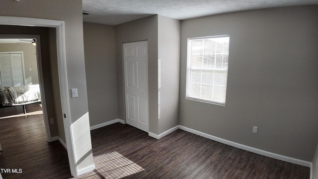 unfurnished bedroom with a textured ceiling, dark hardwood / wood-style floors, and a closet