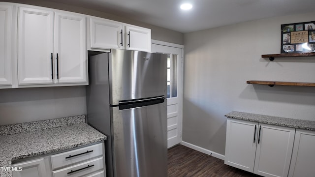 kitchen featuring light stone countertops, stainless steel fridge, white cabinetry, and dark wood-type flooring