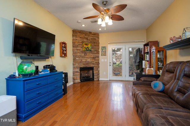 living room with a stone fireplace, ceiling fan, and light hardwood / wood-style floors