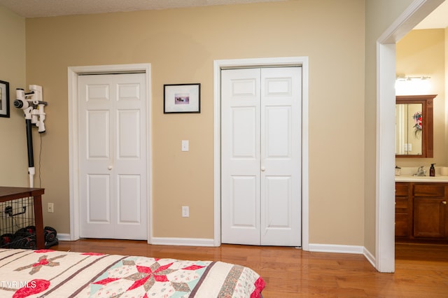 bedroom with sink, light wood-type flooring, a textured ceiling, and ensuite bath