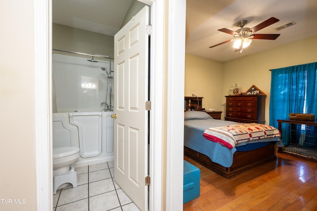 bedroom featuring ceiling fan, ensuite bathroom, a textured ceiling, and light hardwood / wood-style flooring