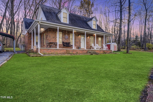 cape cod home featuring a carport, a porch, a storage shed, and a yard