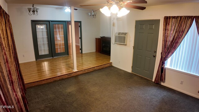 carpeted spare room with a fireplace, french doors, and ceiling fan with notable chandelier