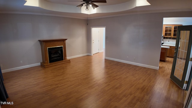 unfurnished living room featuring ceiling fan, light wood-type flooring, and a raised ceiling