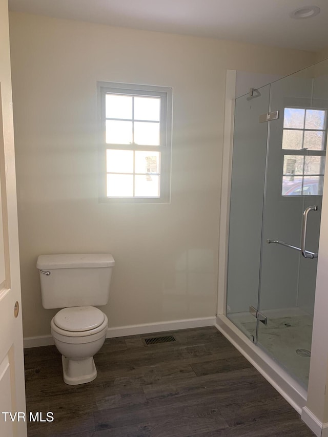 bathroom featuring hardwood / wood-style floors, a healthy amount of sunlight, an enclosed shower, and toilet