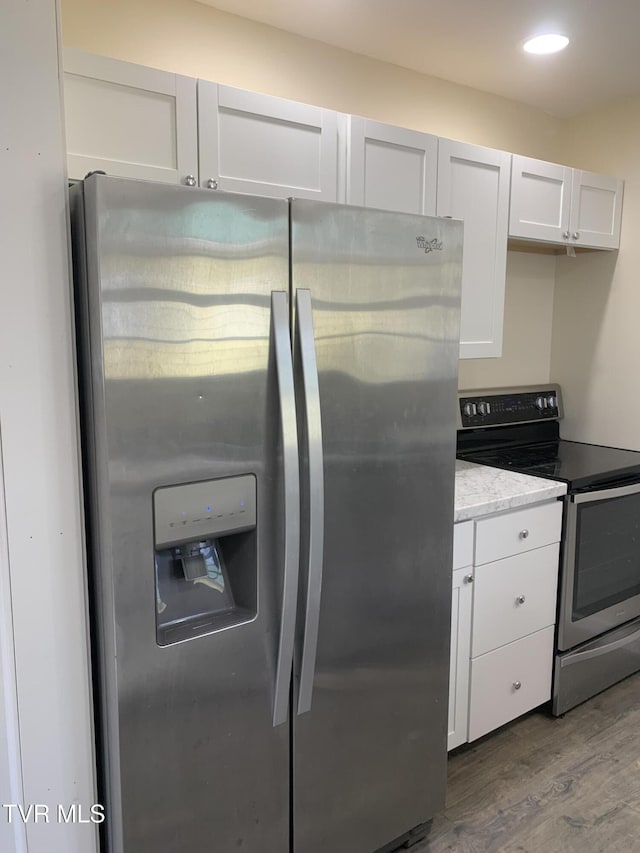 kitchen with stainless steel appliances, white cabinetry, and light hardwood / wood-style floors