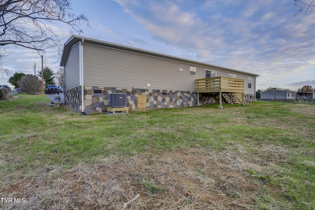 back of house with central air condition unit, a deck, and a lawn