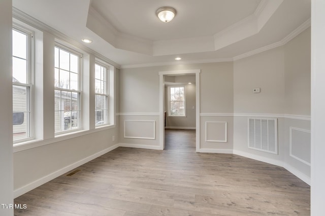 empty room featuring a raised ceiling, crown molding, and light wood-type flooring