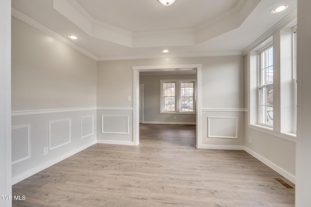 empty room with crown molding, a tray ceiling, and light hardwood / wood-style flooring