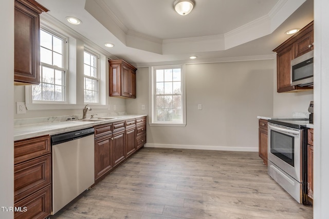 kitchen with ornamental molding, stainless steel appliances, a raised ceiling, sink, and light hardwood / wood-style floors