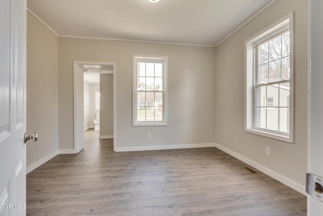 empty room with light hardwood / wood-style floors, ornamental molding, and a wealth of natural light