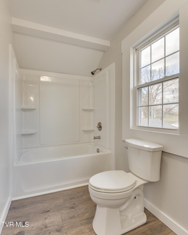 bathroom with hardwood / wood-style floors, washtub / shower combination, lofted ceiling, and toilet