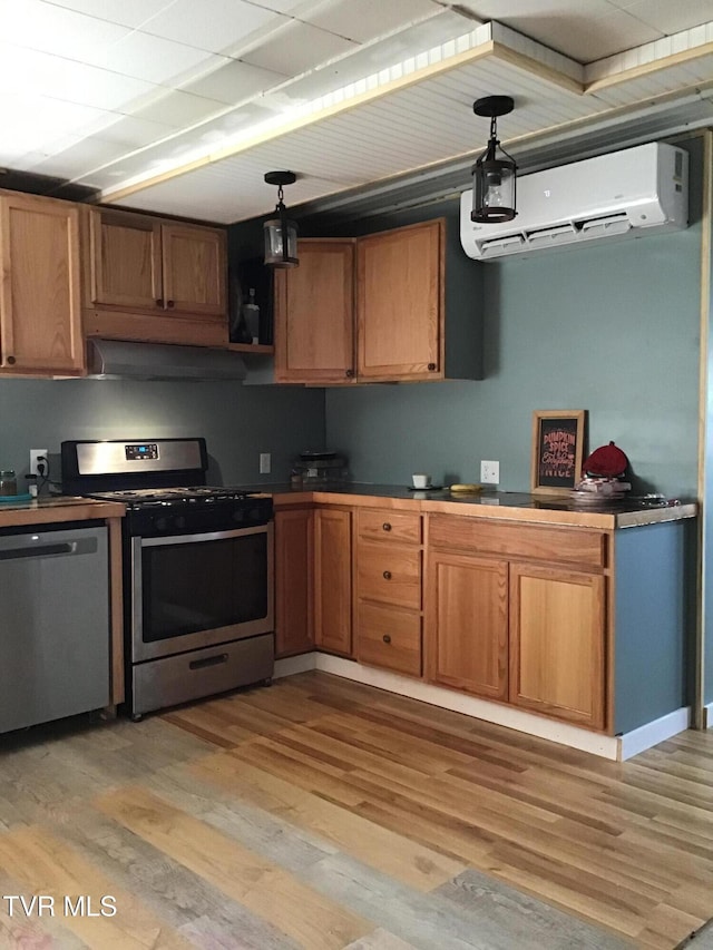 kitchen with appliances with stainless steel finishes, pendant lighting, a wall unit AC, and light hardwood / wood-style flooring