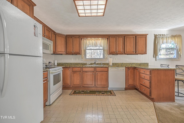 kitchen featuring white appliances, dark stone counters, sink, a textured ceiling, and a kitchen bar