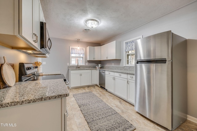 kitchen with light stone countertops, a textured ceiling, appliances with stainless steel finishes, white cabinetry, and hanging light fixtures