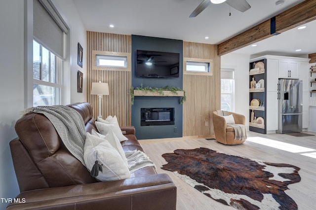 living room featuring a large fireplace, ceiling fan, light hardwood / wood-style flooring, and beamed ceiling