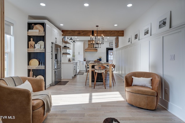 living room featuring beam ceiling, light hardwood / wood-style floors, and a notable chandelier