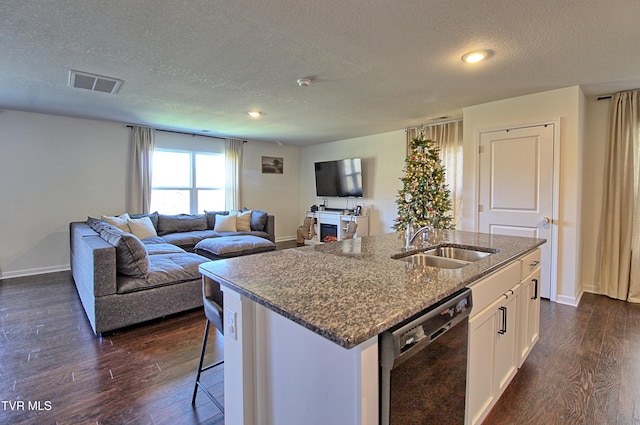 kitchen with white cabinets, dark stone countertops, black dishwasher, and a kitchen island with sink