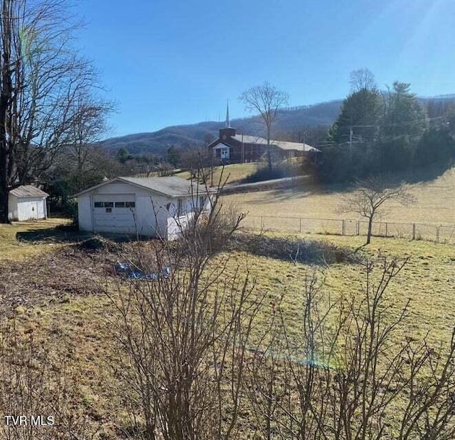 view of yard with a detached garage, fence, a mountain view, and an outbuilding