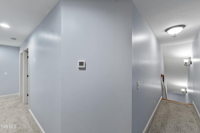 hallway with light colored carpet and a textured ceiling