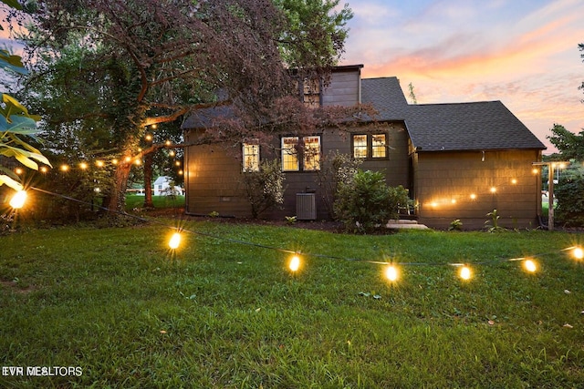 back house at dusk with a yard and central AC