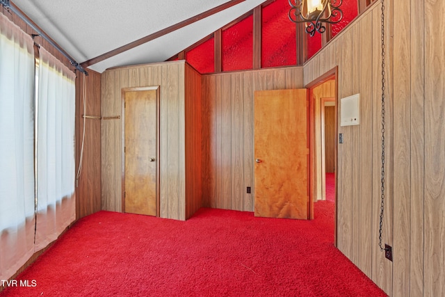 unfurnished bedroom featuring carpet flooring, wood walls, lofted ceiling, and a textured ceiling