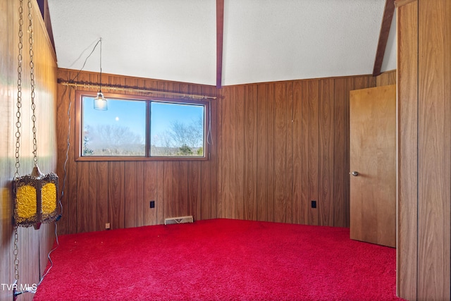 carpeted spare room with a textured ceiling, wooden walls, and lofted ceiling