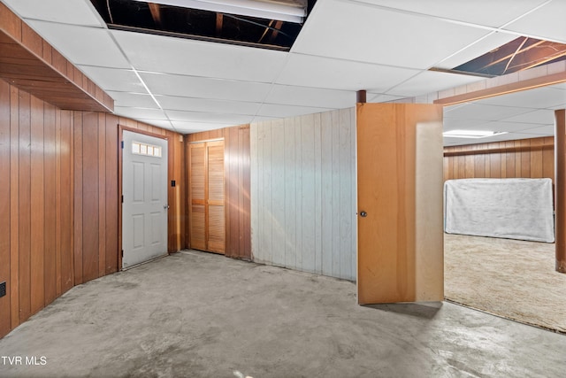 basement featuring a paneled ceiling and wood walls