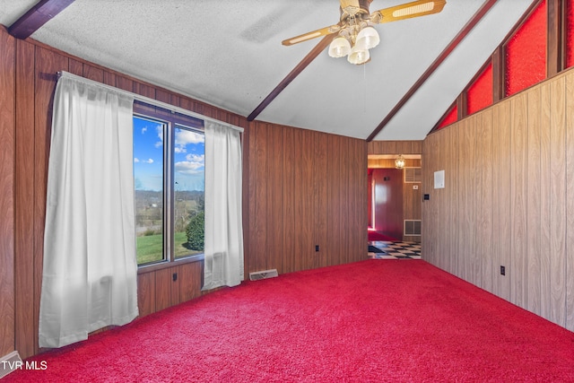 spare room featuring wooden walls, vaulted ceiling with beams, ceiling fan, a textured ceiling, and carpet floors