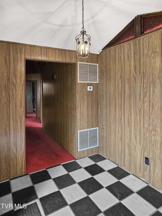 interior space with lofted ceiling, a textured ceiling, wooden walls, and a chandelier