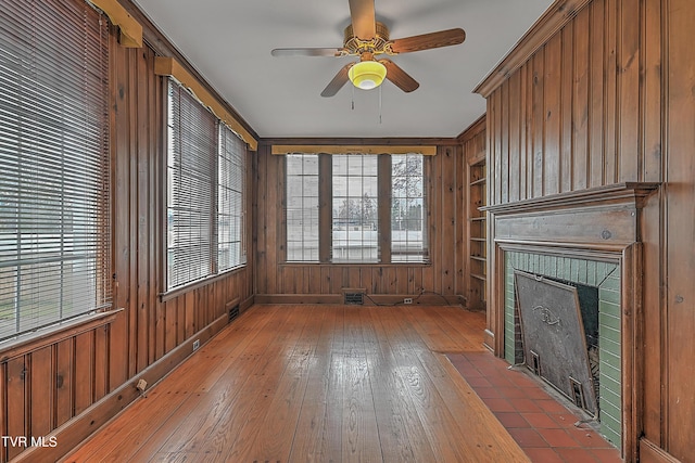 unfurnished living room featuring a fireplace, ceiling fan, hardwood / wood-style floors, and wooden walls