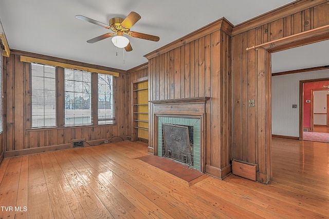 unfurnished living room with ceiling fan, built in shelves, ornamental molding, a fireplace, and light hardwood / wood-style floors