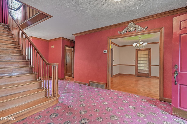 foyer with a chandelier, a textured ceiling, light wood-type flooring, and crown molding