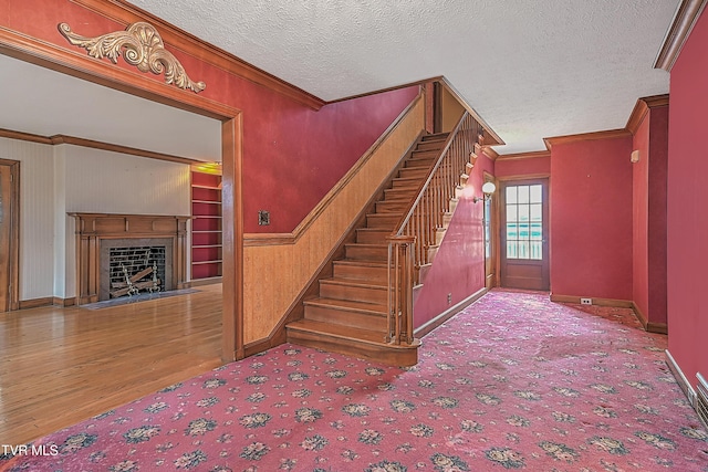 staircase featuring hardwood / wood-style floors, built in features, crown molding, and a textured ceiling