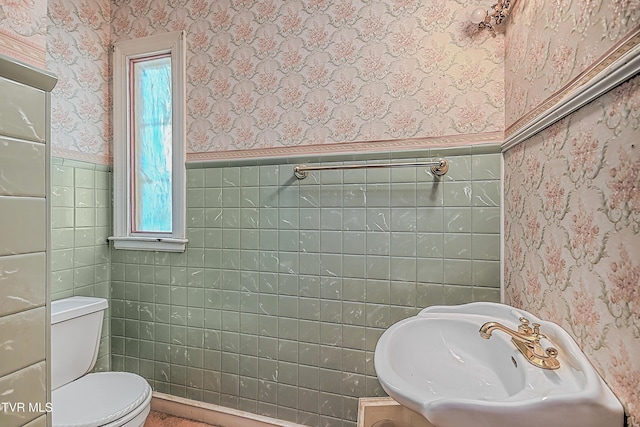 bathroom featuring toilet, sink, a wealth of natural light, and tile walls