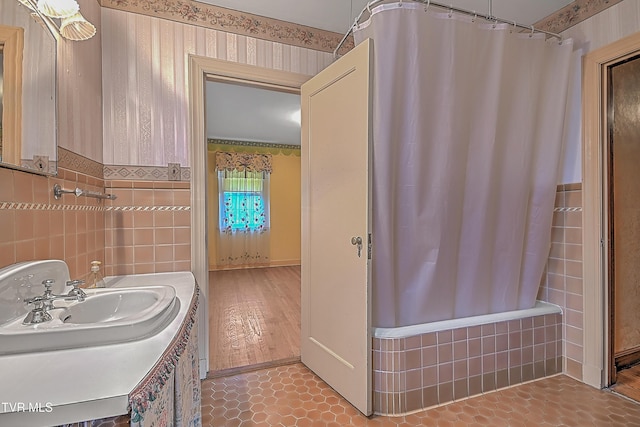 bathroom with hardwood / wood-style flooring, tile walls, shower / bath combo with shower curtain, and sink