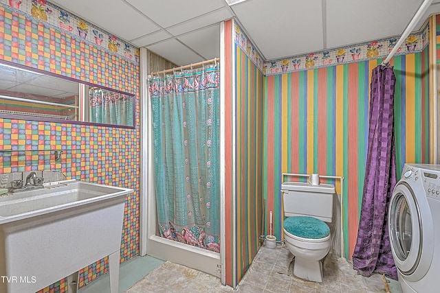 bathroom featuring a drop ceiling, toilet, sink, and washer / clothes dryer