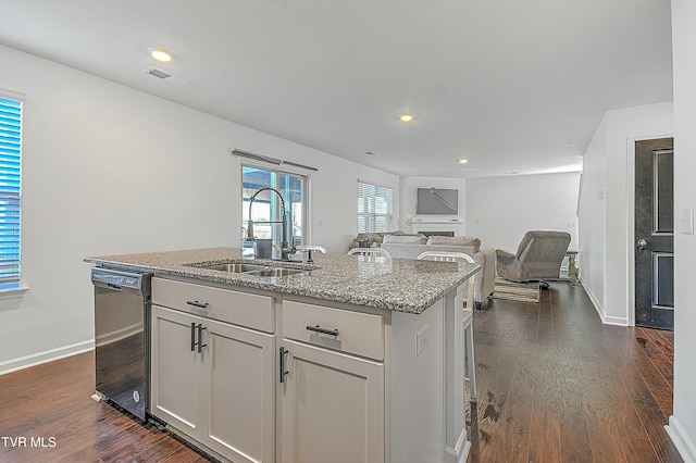 kitchen with light stone countertops, sink, dark wood-type flooring, black dishwasher, and a kitchen island with sink