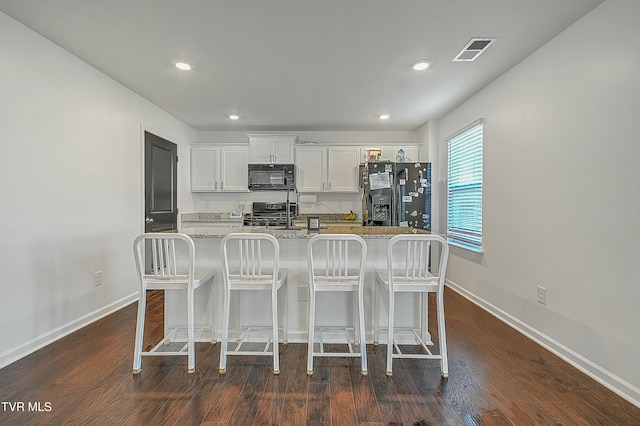 kitchen featuring light stone countertops, white cabinetry, dark hardwood / wood-style flooring, a breakfast bar, and black appliances