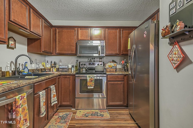 kitchen featuring dark stone counters, sink, stainless steel appliances, and light hardwood / wood-style floors