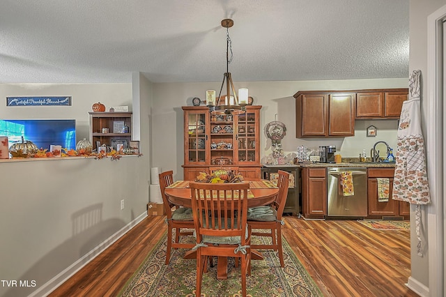 dining space with sink, dark wood-type flooring, a textured ceiling, and an inviting chandelier