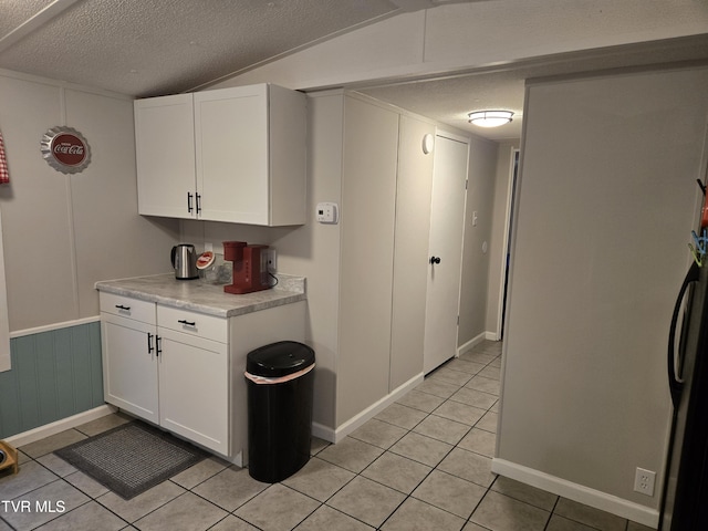 kitchen with white cabinets, a textured ceiling, lofted ceiling, and light tile patterned flooring