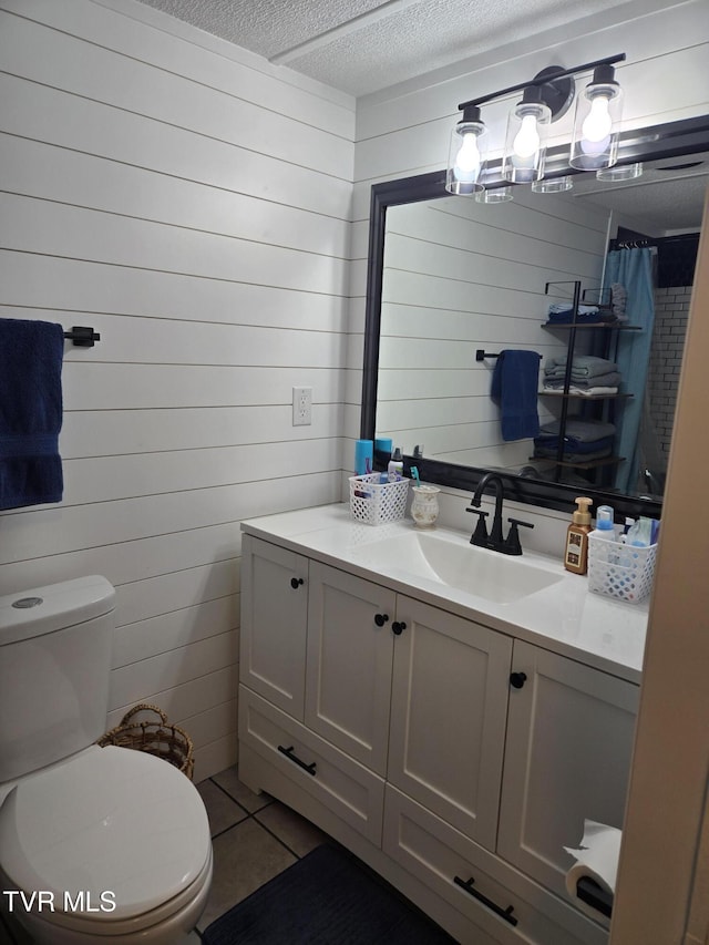 bathroom with tile patterned floors, vanity, a textured ceiling, toilet, and wood walls